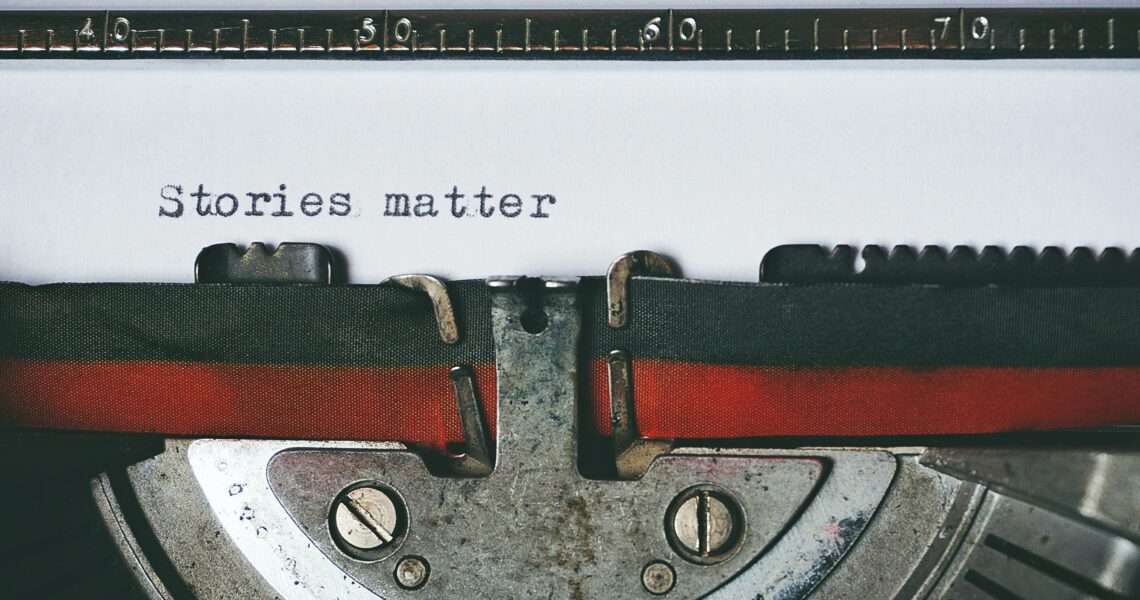 An old-fashioned typewriter holds a piece of white paper on which the words "stories matter" are typed. | Photo by Suzy Hazelwood